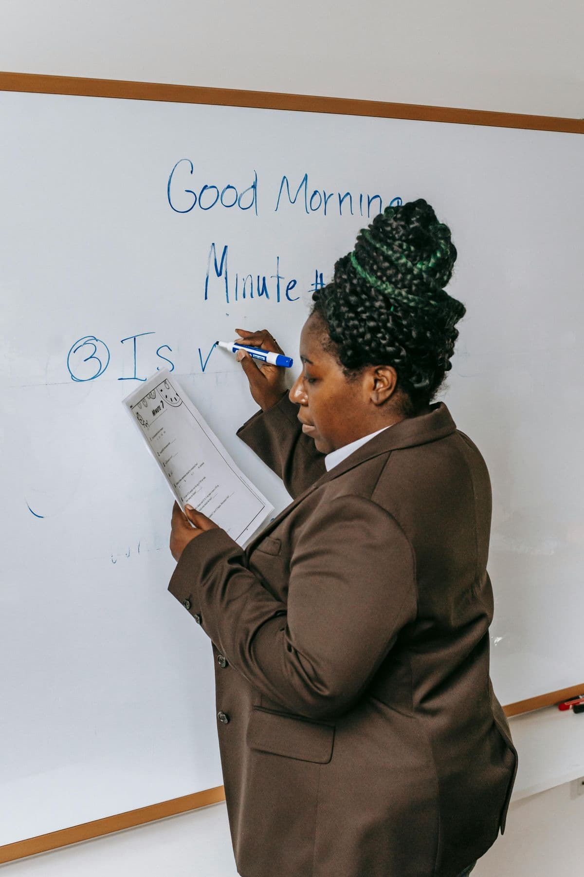 A trainer writing on a classroom whiteboard while holding lesson notes