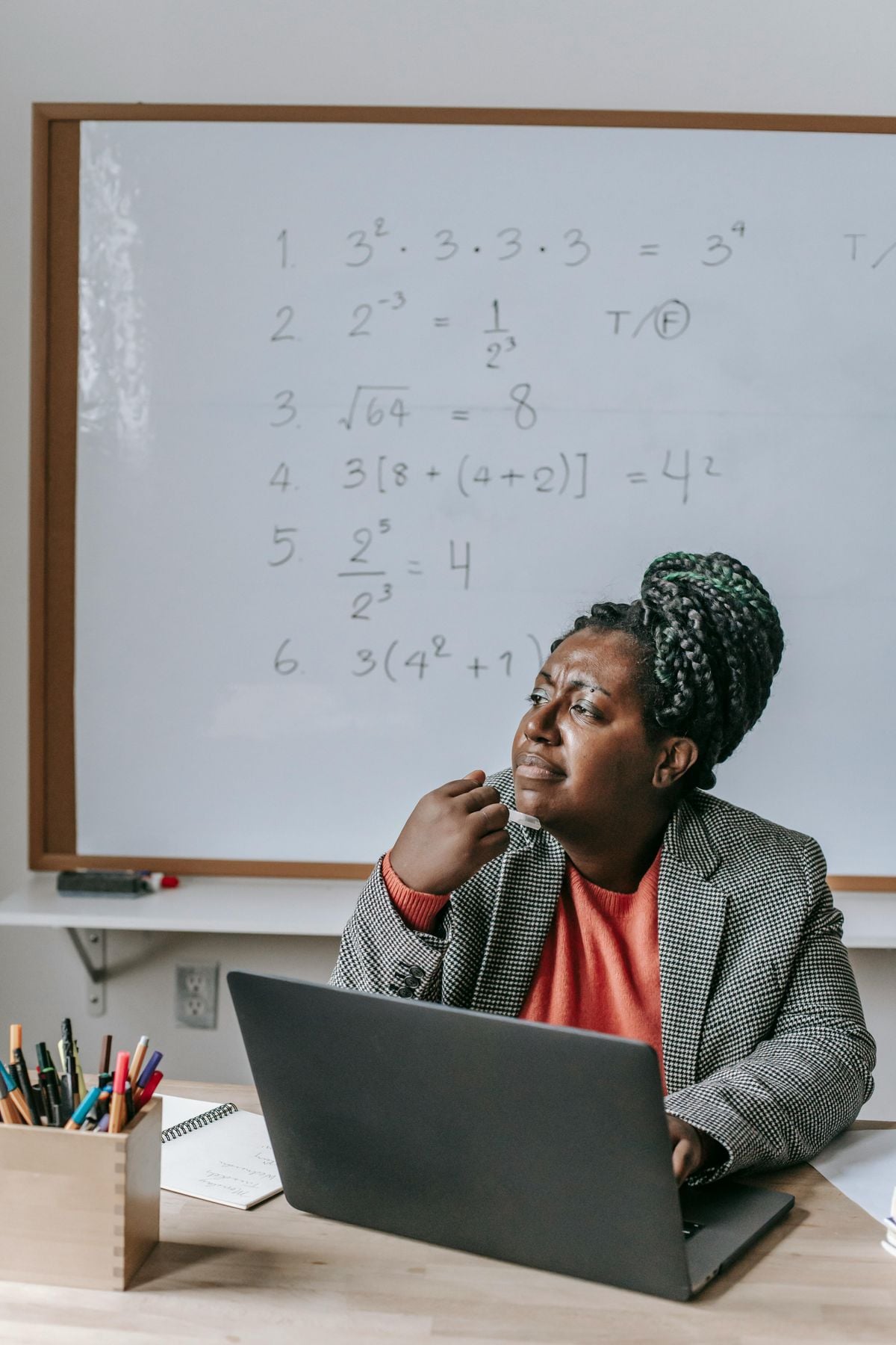 A trainer writing session notes on a classroom whiteboard while holding planning papers